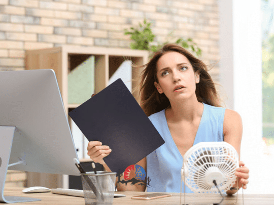 woman fanning herself because her AC is broken and she's too hot at home